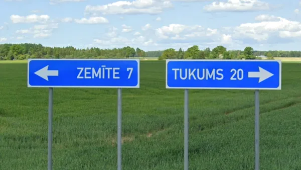 Синие латвийские дорожные указатели с белыми буквами на перекрёстке